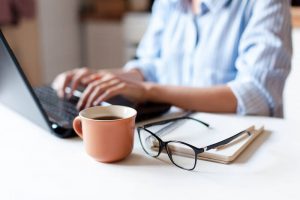 Person works on laptop with a cup of coffee.