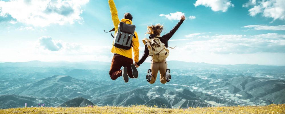 Hikers with backpacks jumping with arms up on top of a mountain Hikers with backpacks jumping with arms up on top of a mountain - Couple of young happy travelers climbing the peak - Family, travel and adventure concept