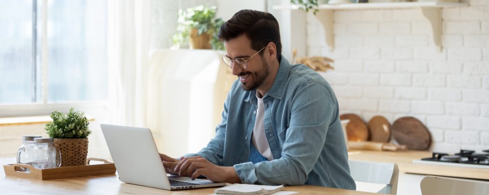 Smiling,Young,Man,Working,On,Laptop,In,Modern,Kitchen,,Checking