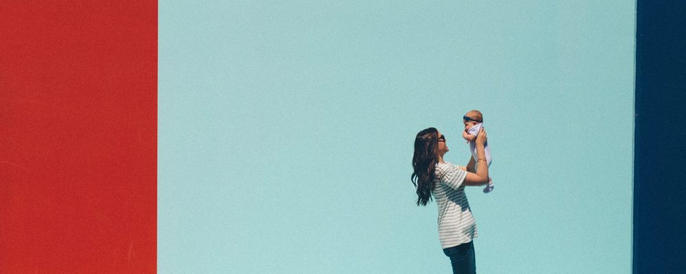 A woman walks with her baby in front of a bright mural.