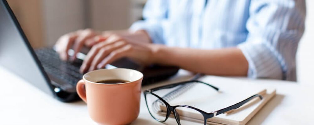 financial-guide-to-starting-a-new-job Person works on laptop with a cup of coffee.