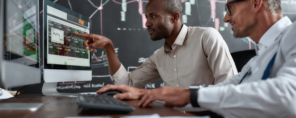 Two,Diverse,Colleagues,Traders,Talking,To,Each,Other,,Looking,At