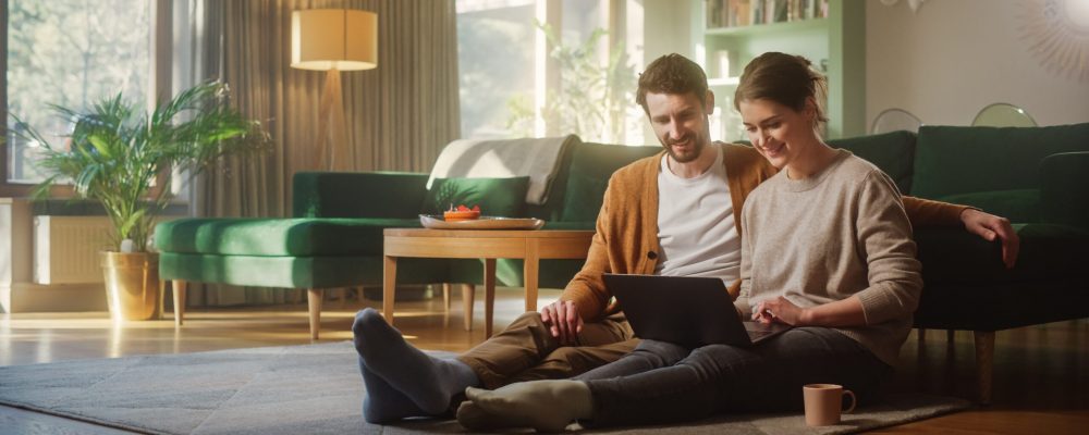 Couple,Use,Laptop,Computer,,While,Sitting,On,The,Living,Floor